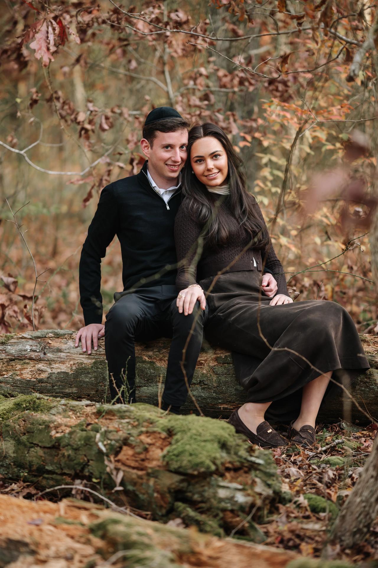 Couple seated together on a moss-covered log during an autumn portrait session