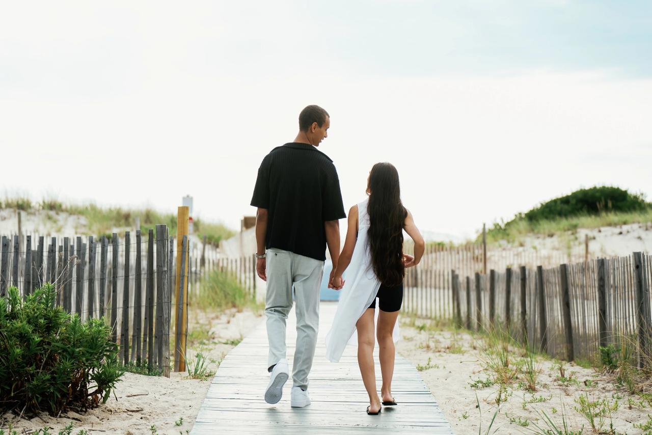 Couple walking hand in hand along a sandy boardwalk toward the beach