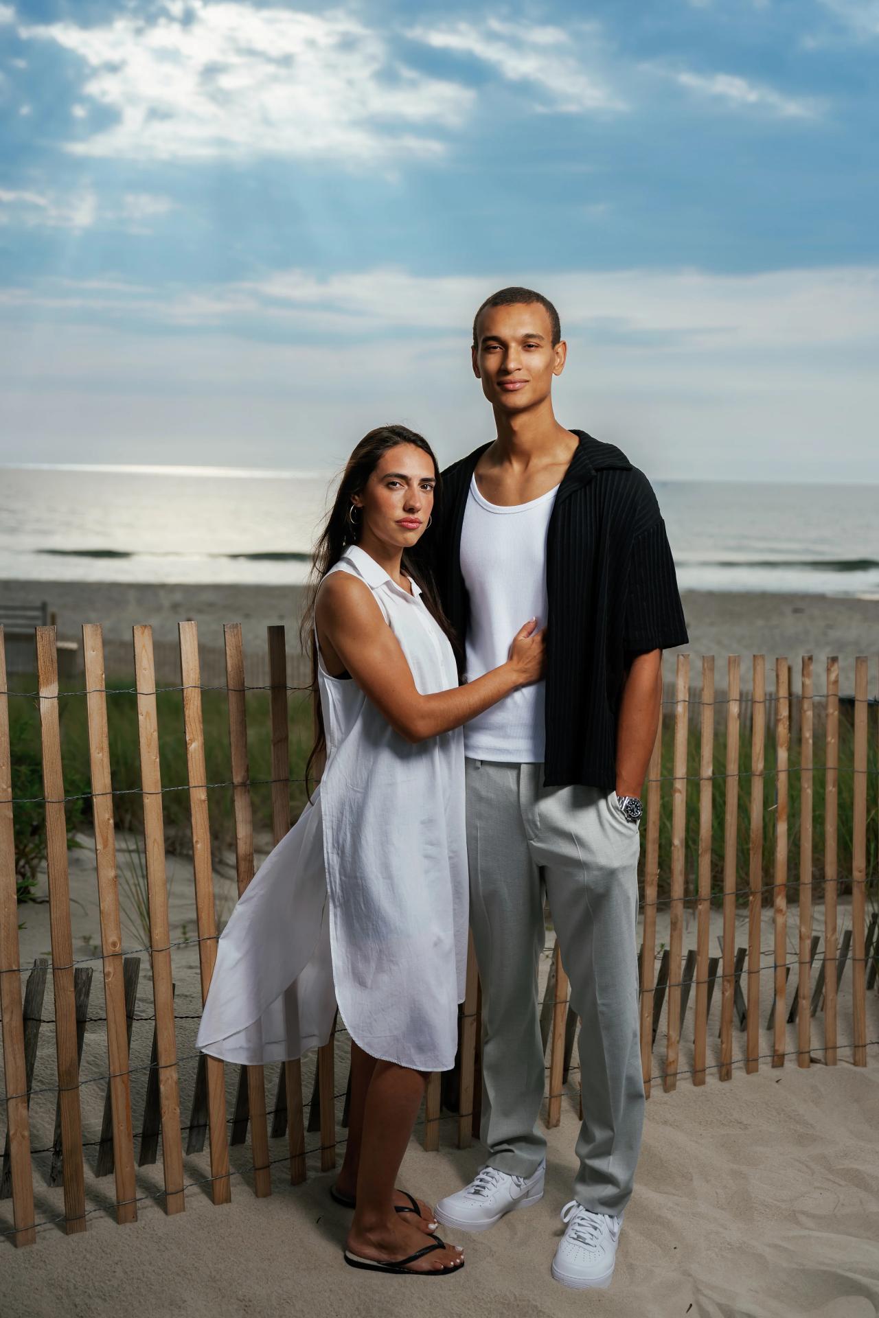 Full-length portrait of a couple beside a dune fence with the ocean behind them