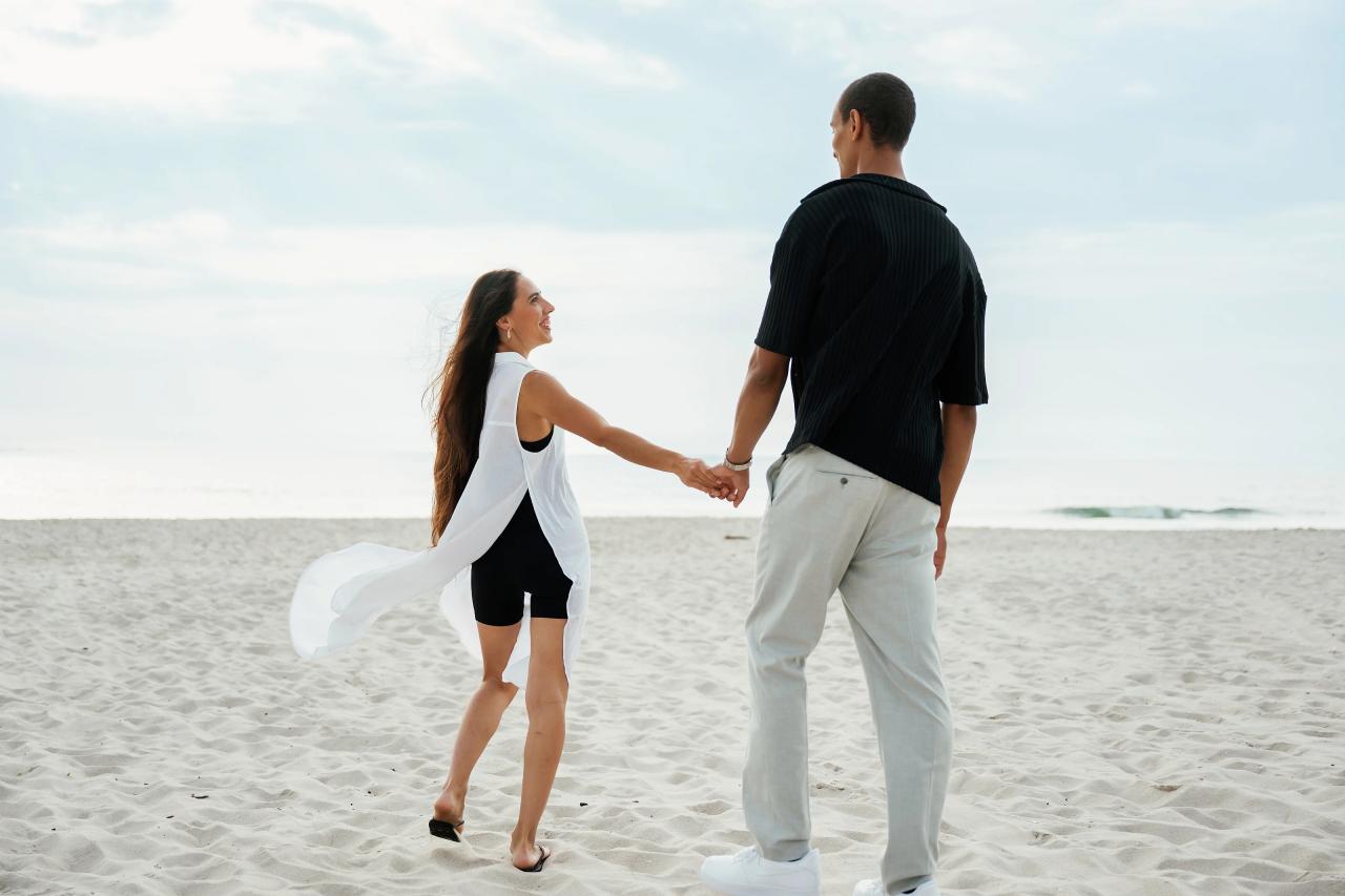 Couple holding hands while walking onto the sand by the ocean