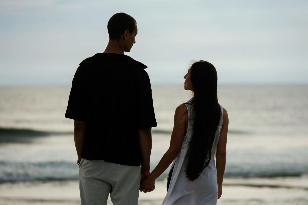 Couple holding hands and looking toward the ocean