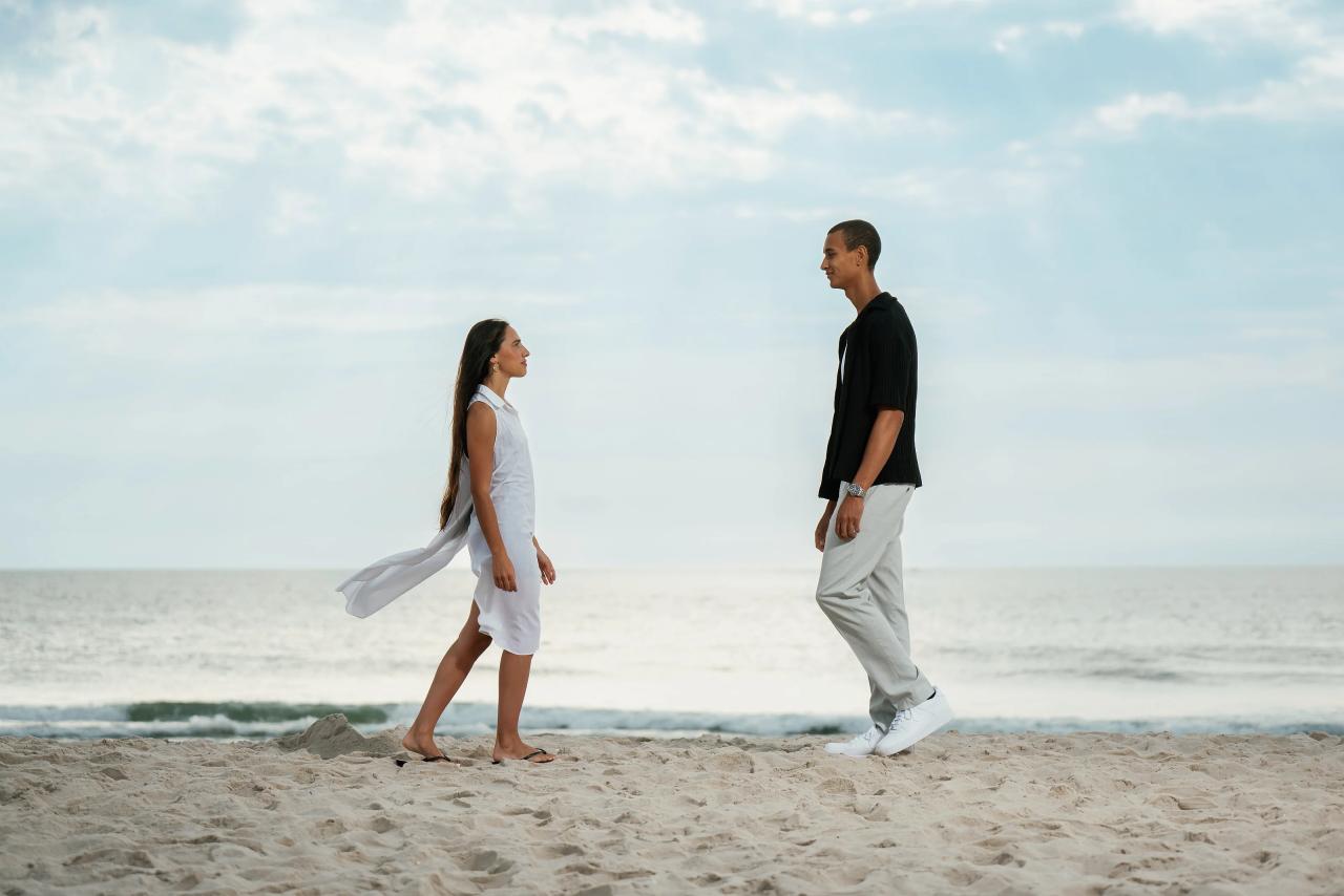 Couple walking toward each other on the beach with waves behind them