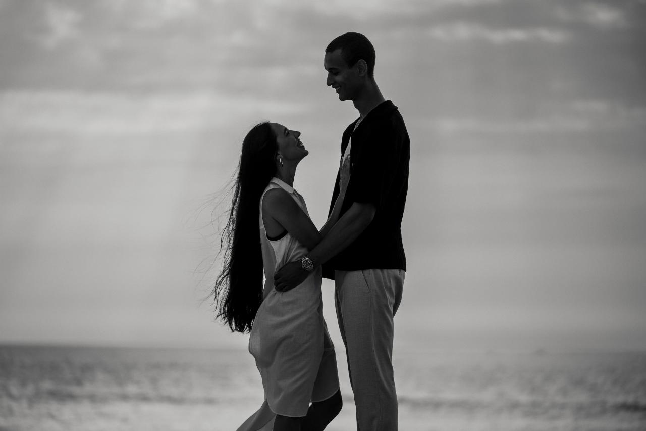 Black-and-white portrait of a couple facing each other on the beach