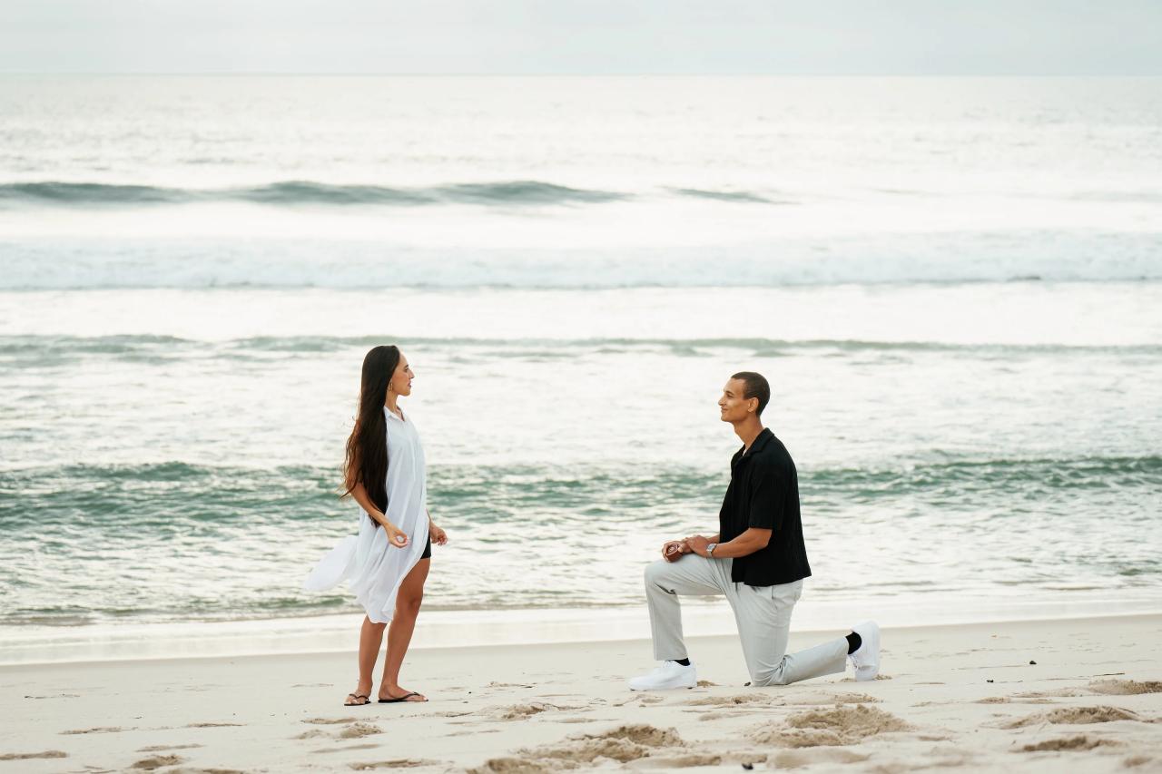 Woman turning toward her partner as he proposes on the sand
