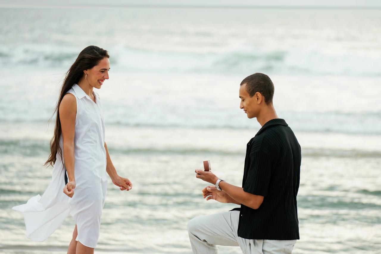 Man holding an engagement ring while proposing beside the ocean