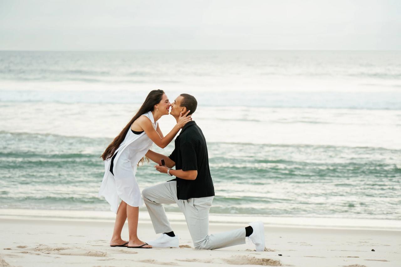 Couple sharing a kiss while the man kneels on the sand