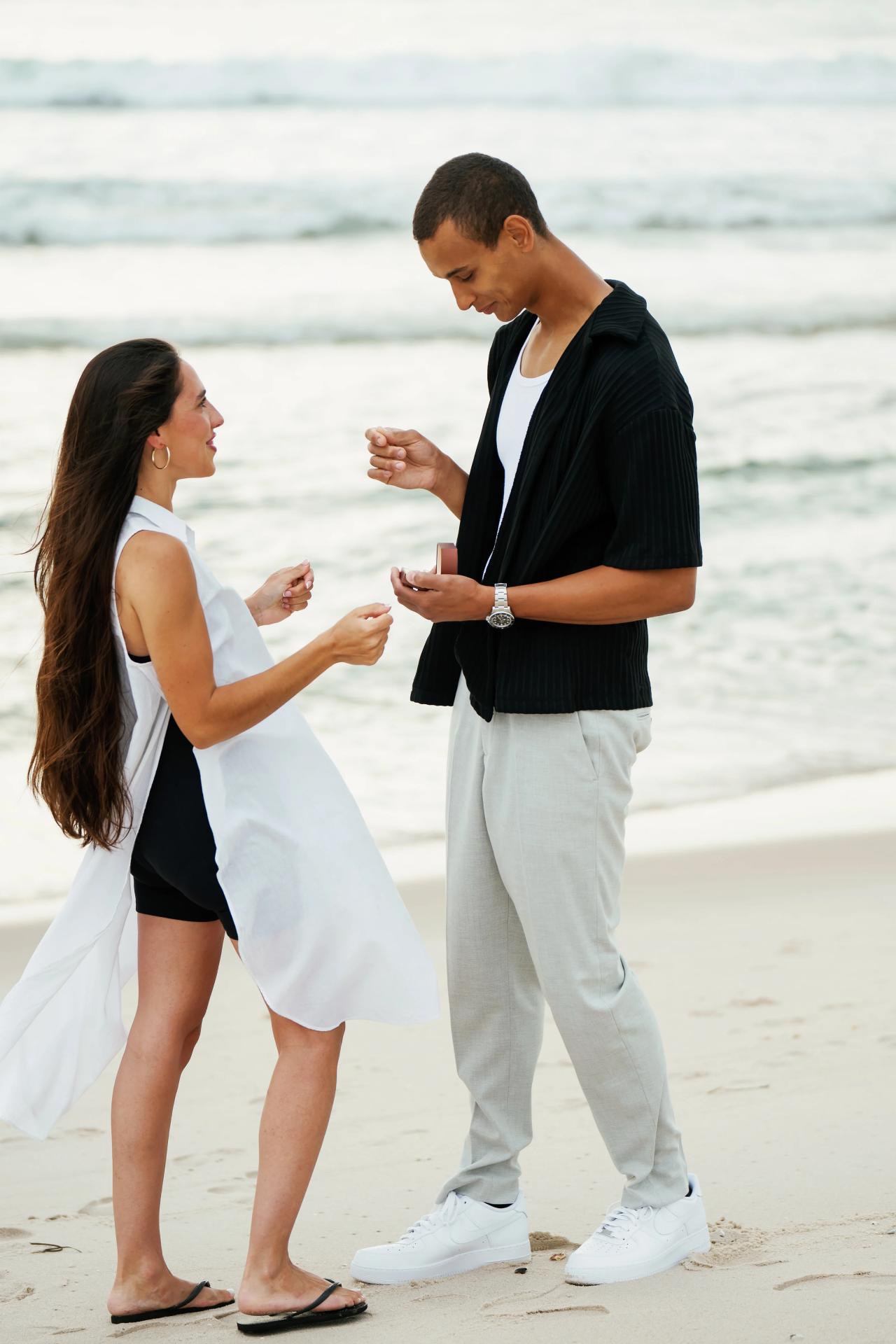 Couple smiling together and looking at the engagement ring by the ocean