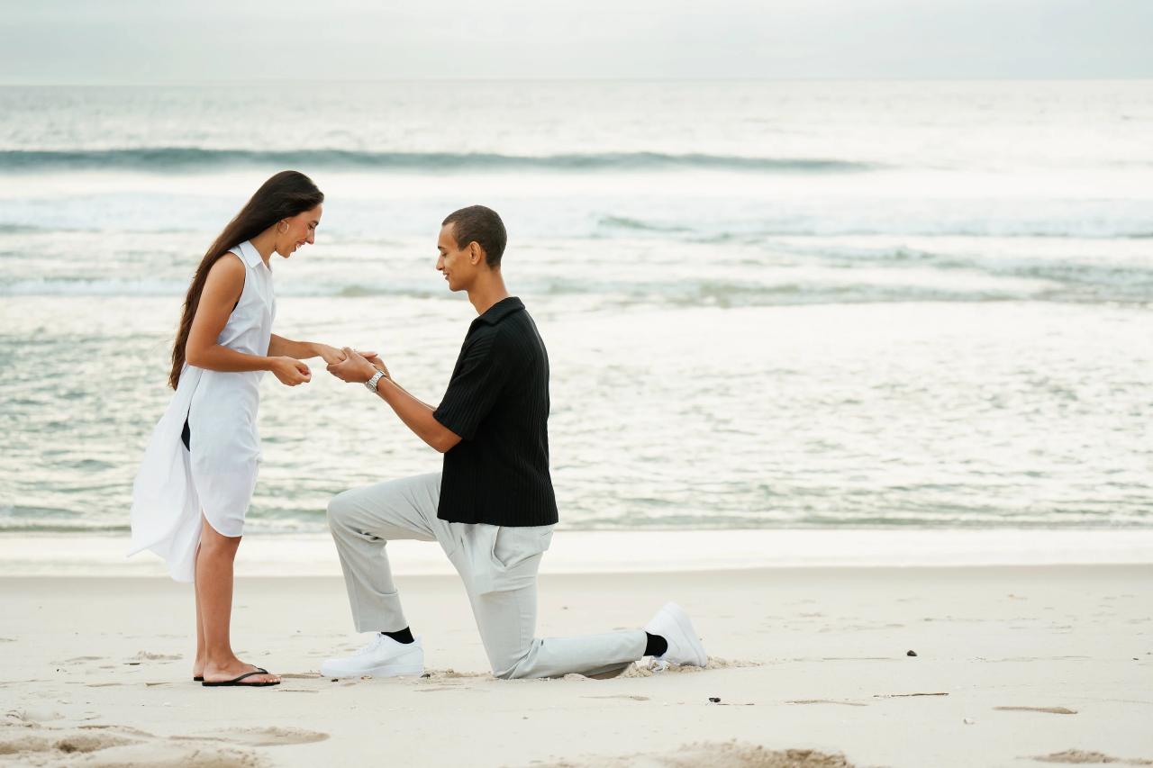 Man placing a ring on his partner’s finger while kneeling on the beach