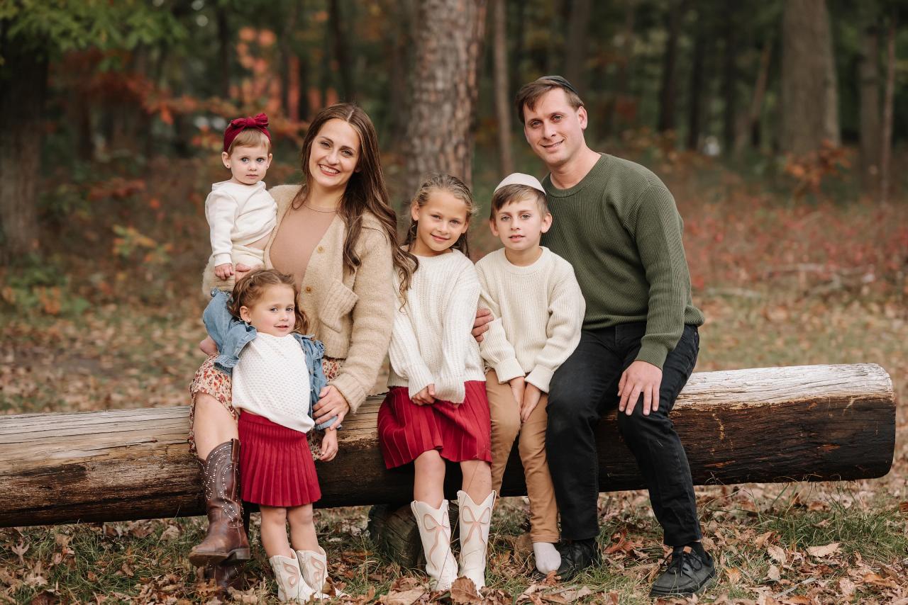 Family of six sitting together on a fallen log in the autumn woods