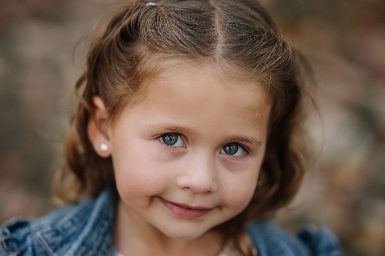 Young girl in a denim jacket smiling during an outdoor family portrait session