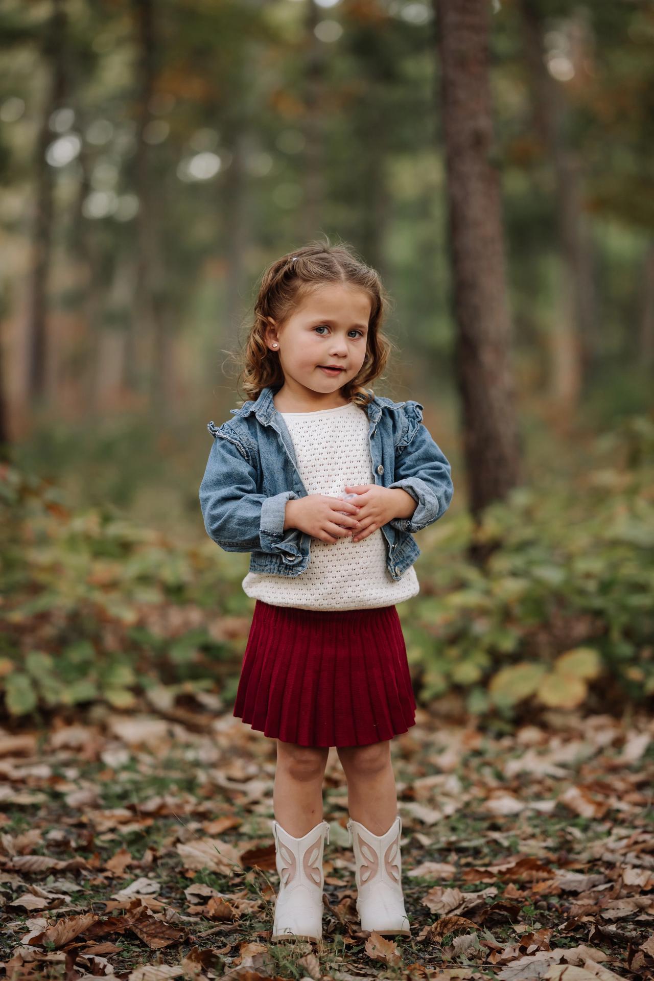 Full-length portrait of a young girl in a red skirt among fallen leaves