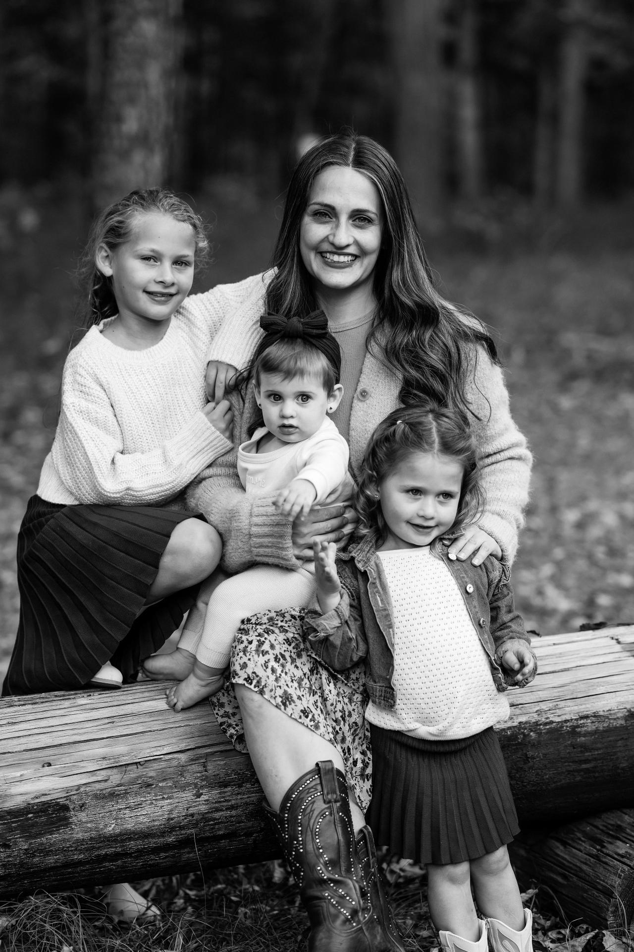 Black-and-white portrait of a mother and her children on a woodland log