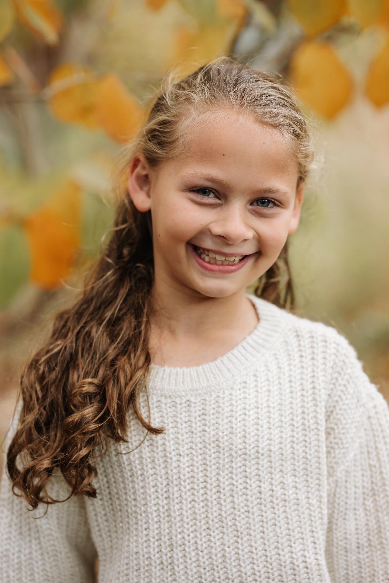Girl smiling beneath golden autumn leaves