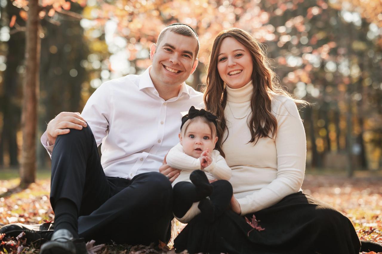 Parents and their baby sitting together among autumn leaves