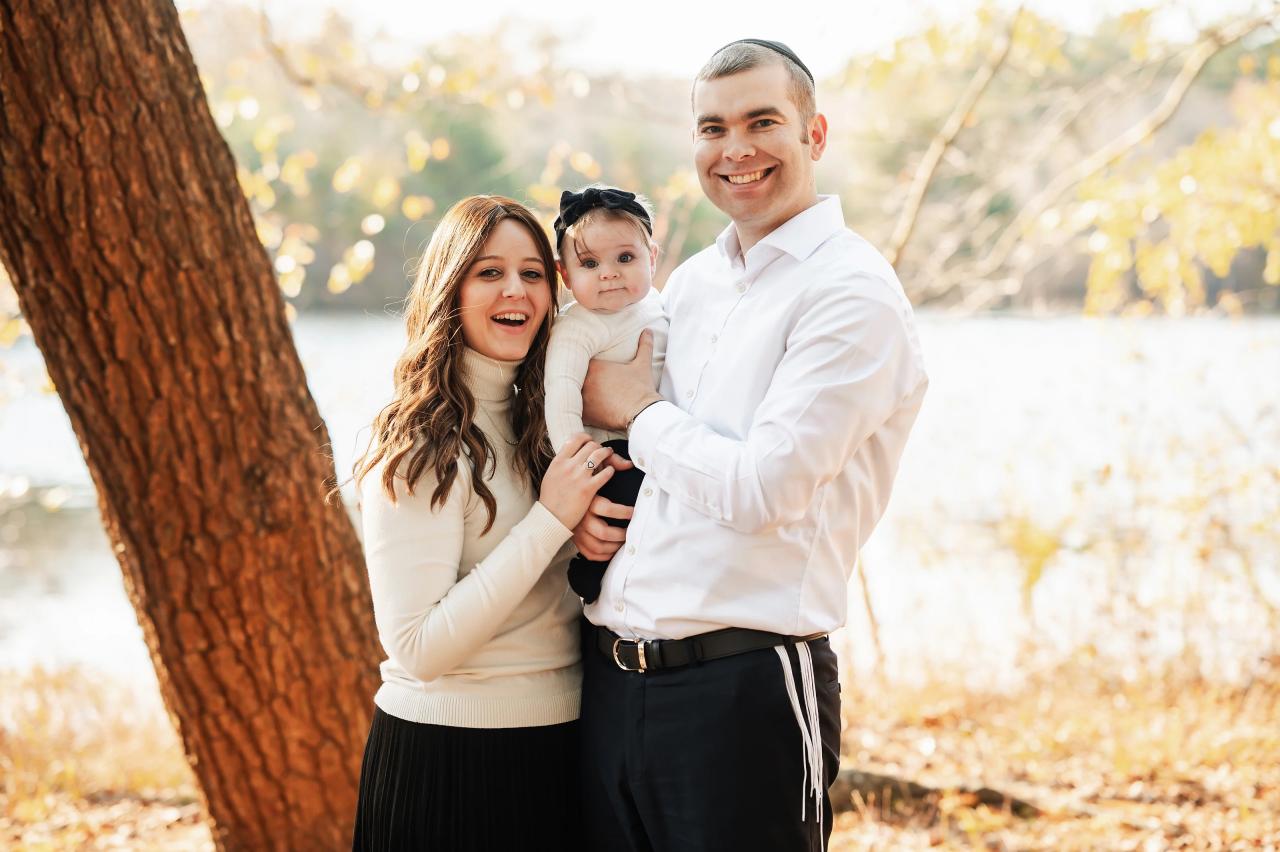 Parents holding their baby beside a tree and lake