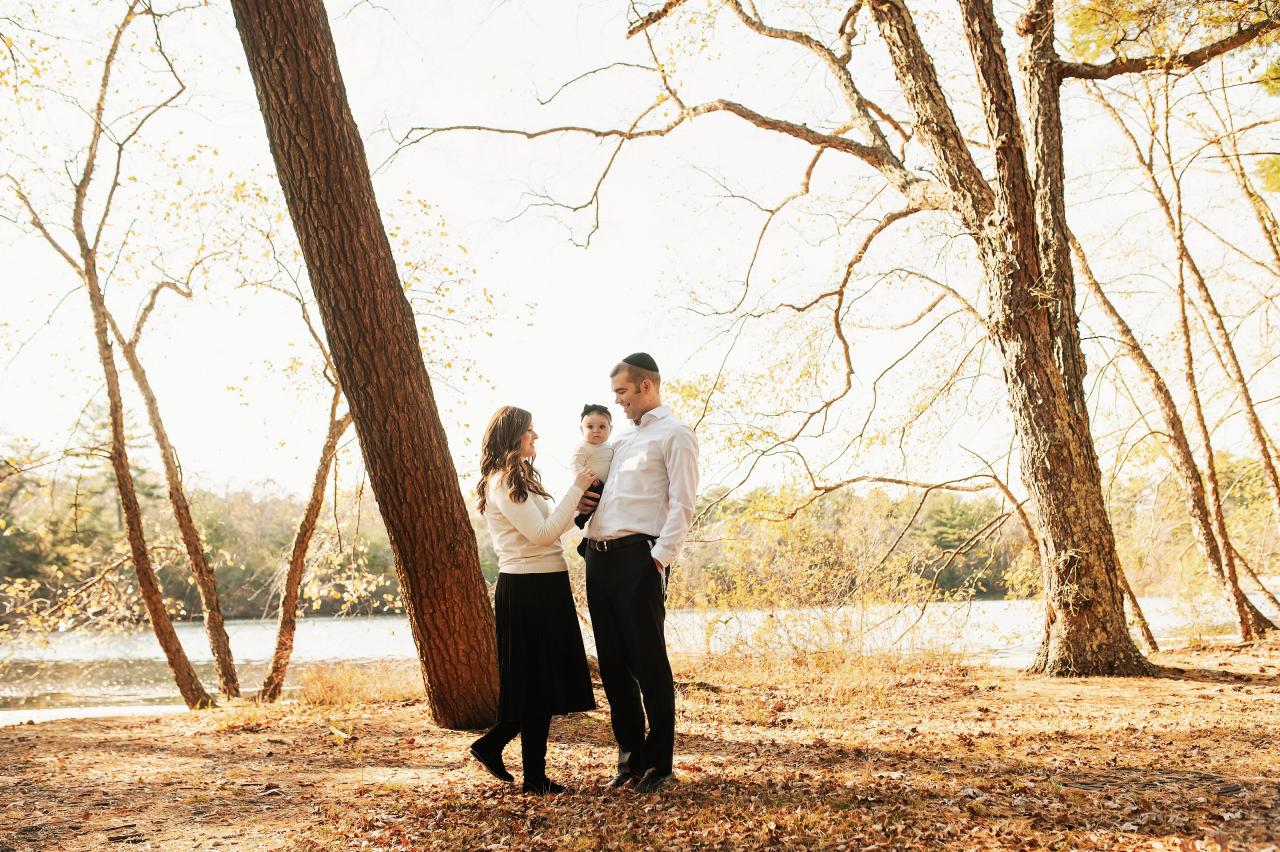 Wide family portrait beneath autumn trees beside the water