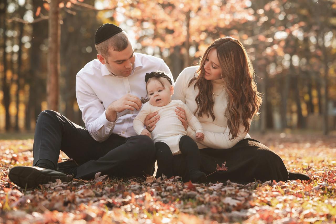 Parents looking at their baby while sitting on fallen leaves