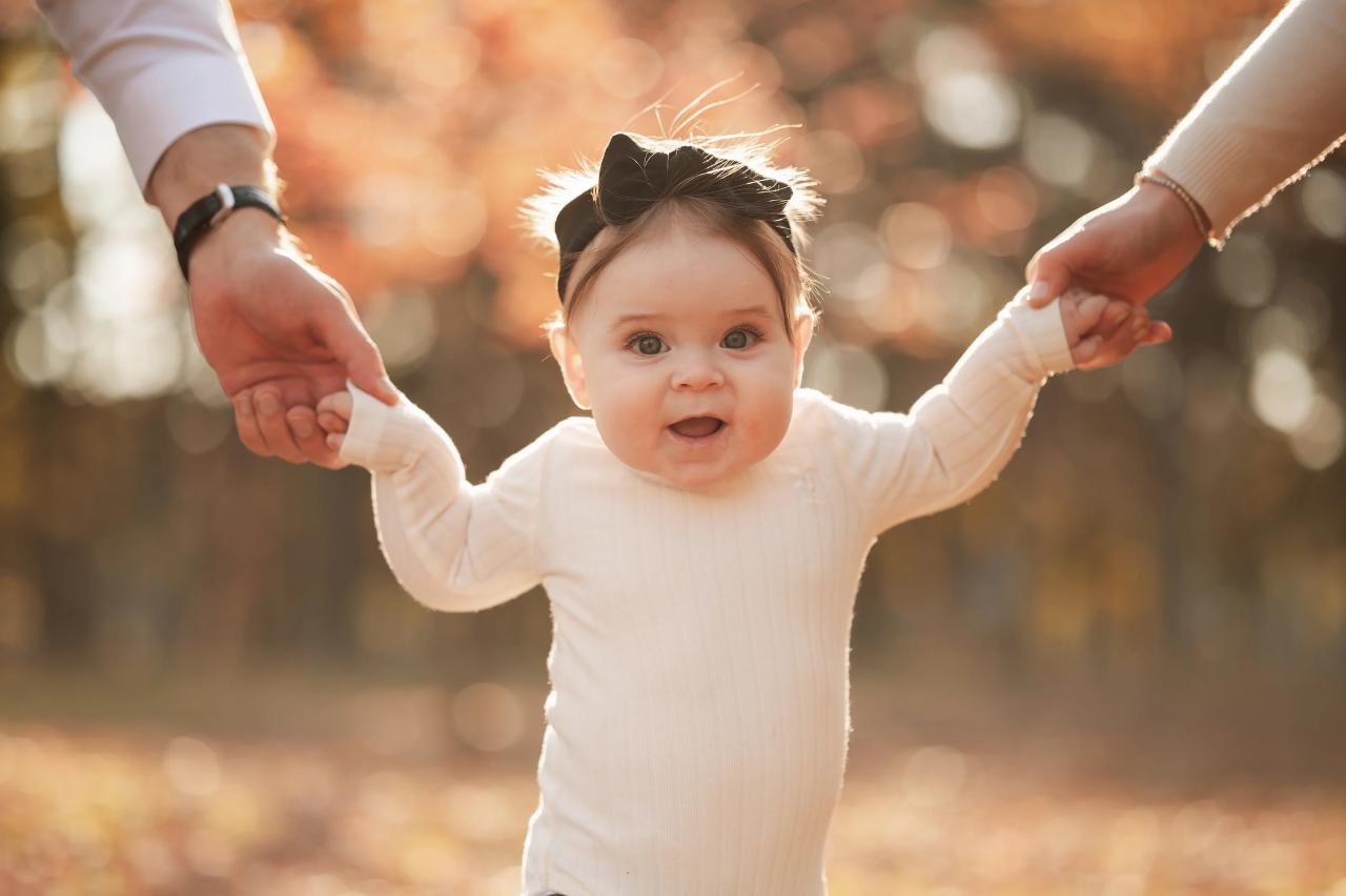 Baby smiling while holding hands with both parents outdoors