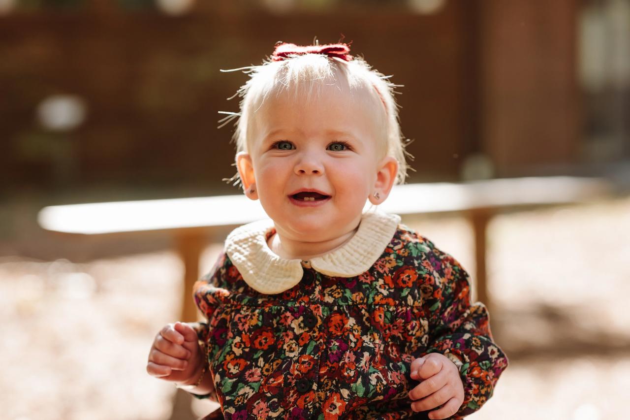 Smiling baby in a floral dress sitting on a wooden railing