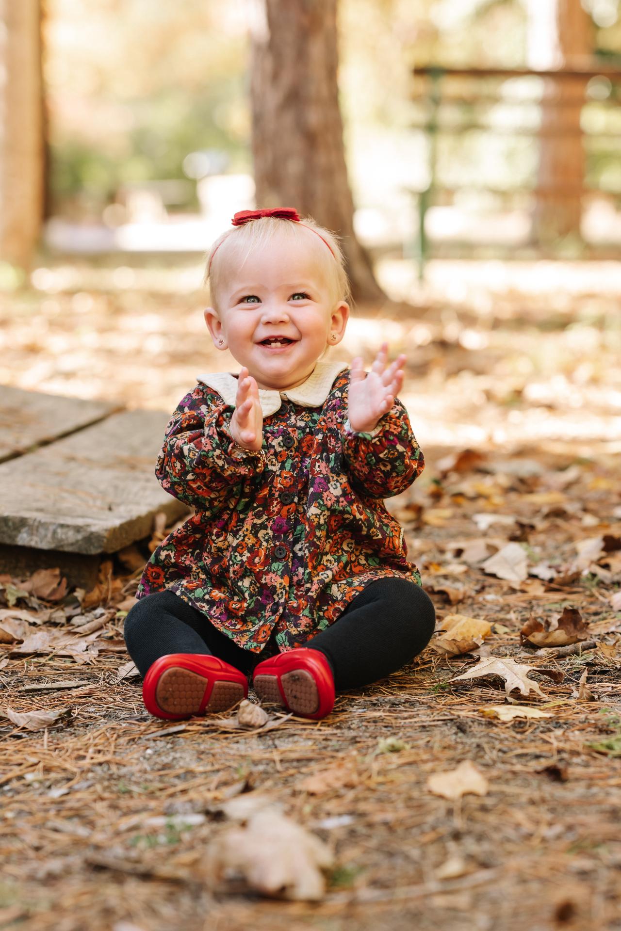 Baby laughing among fallen leaves beside a wooden porch