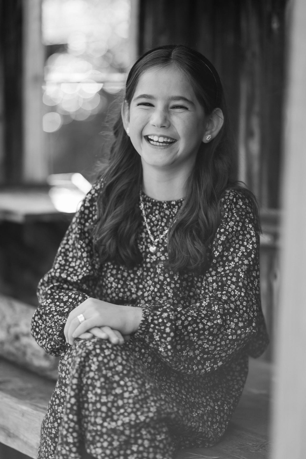 Black-and-white portrait of a smiling girl beside a cabin window