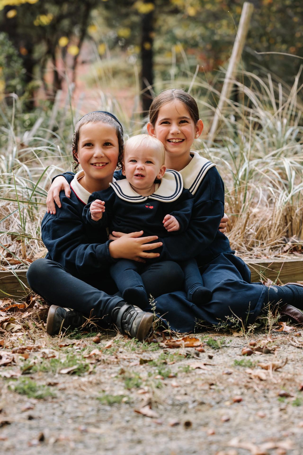 Three siblings sitting together among autumn leaves