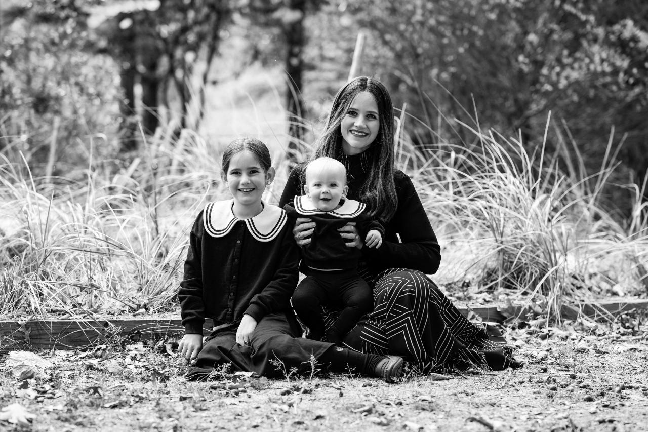 Black-and-white portrait of a mother sitting with her daughters in the woods