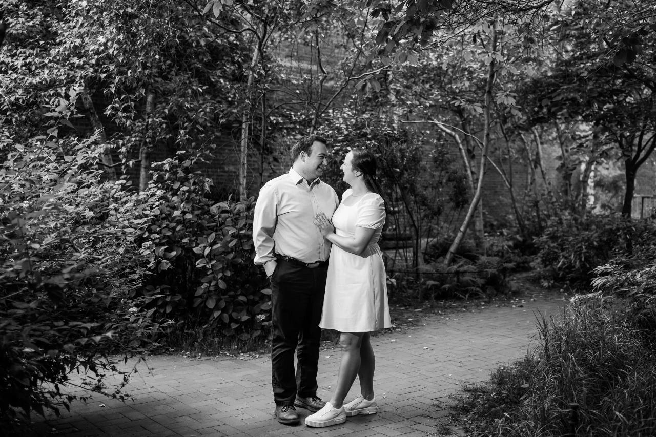 Black-and-white engagement portrait beneath garden trees