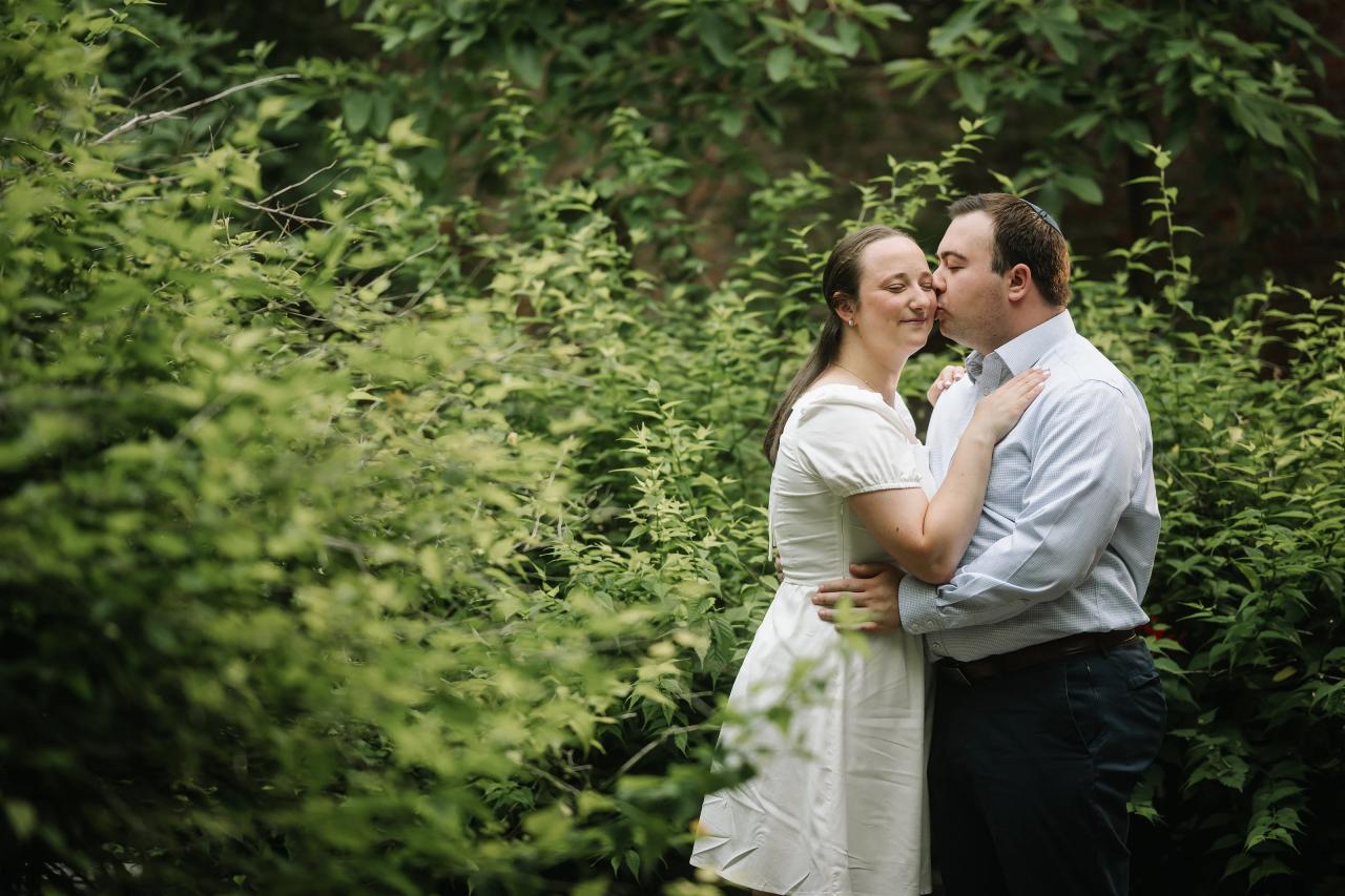 Couple sharing a kiss surrounded by green foliage