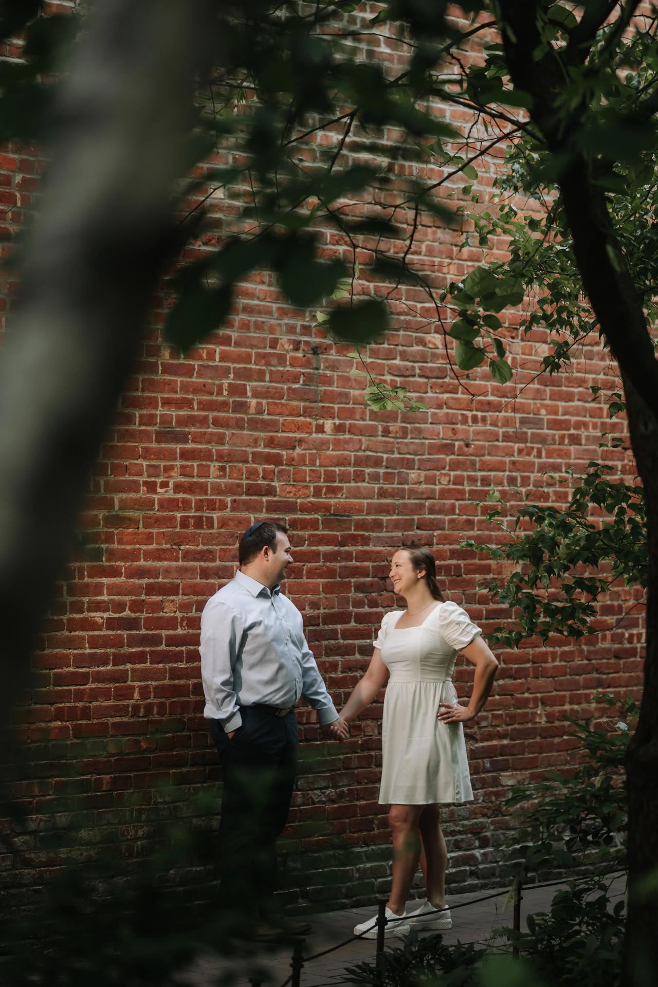Couple holding hands beside a brick wall framed by leaves