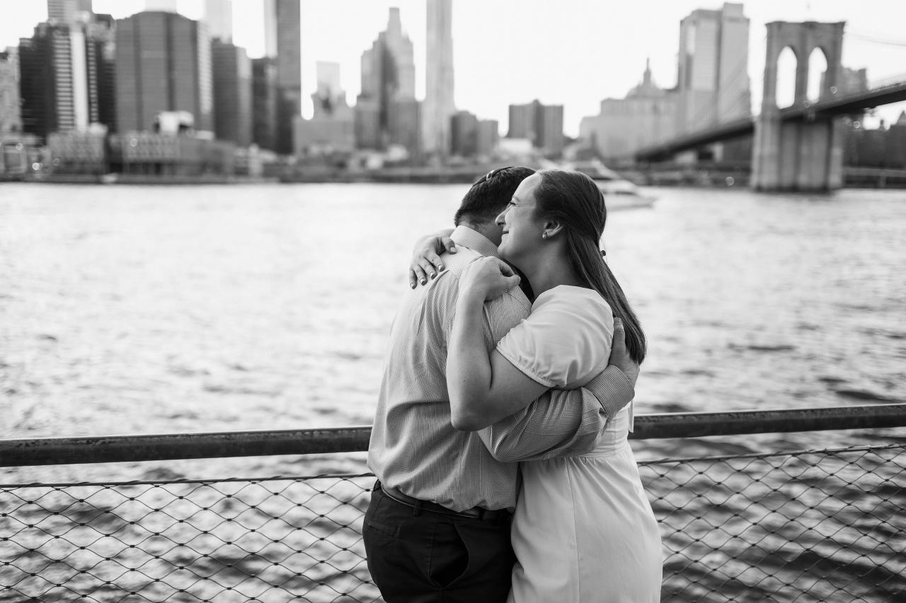 Black-and-white portrait of a couple embracing beside the Brooklyn Bridge