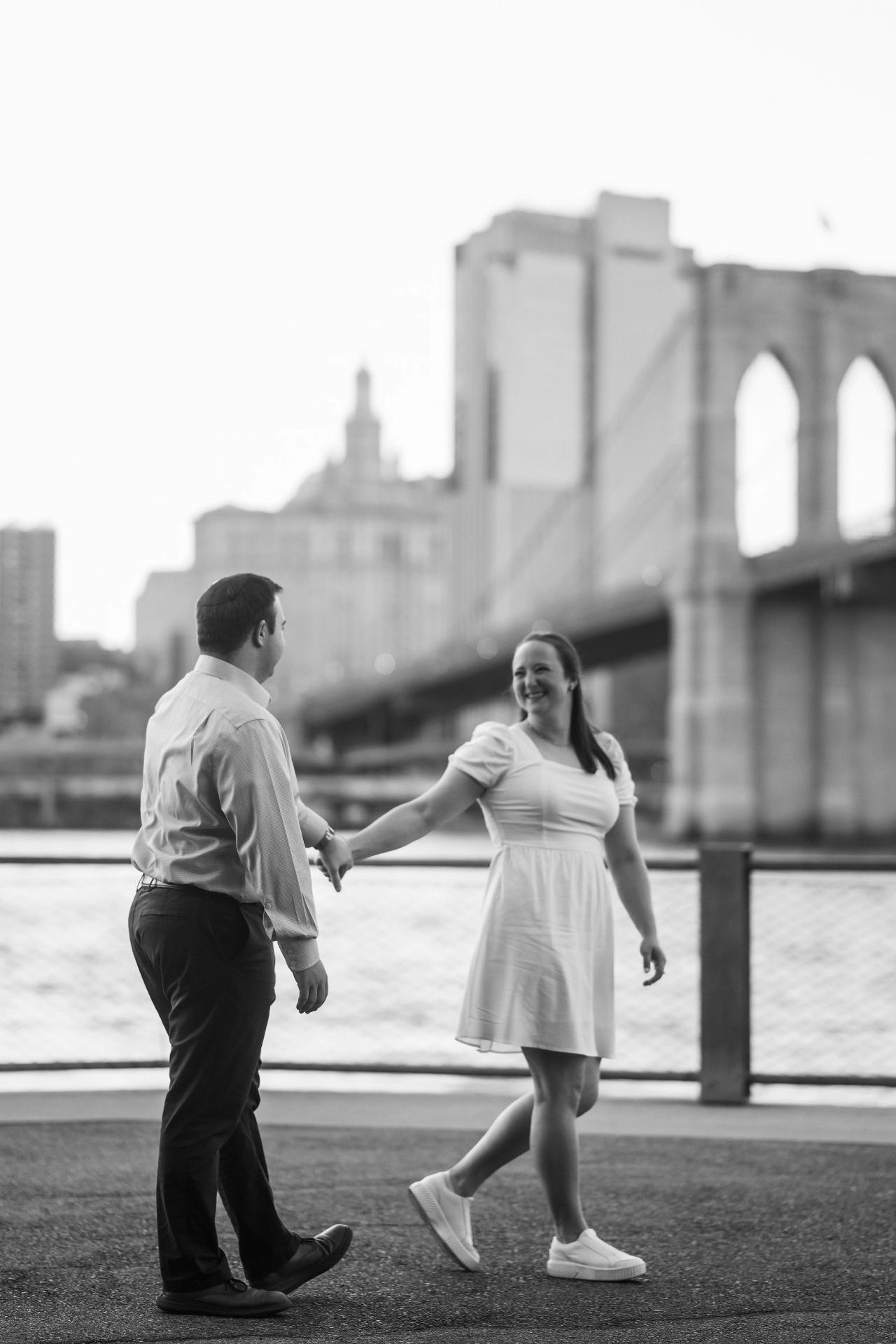 Black-and-white portrait of a couple twirling by the Brooklyn Bridge