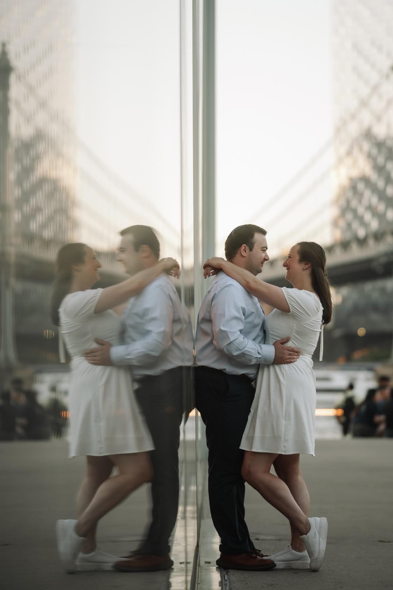 Couple embracing beside a glass reflection with the bridge behind them