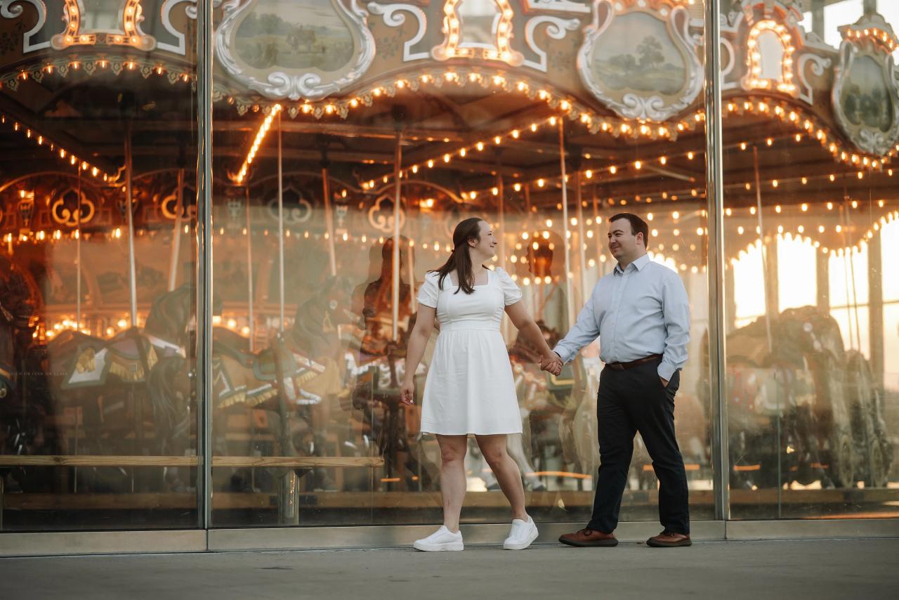Couple holding hands beside a glowing waterfront carousel