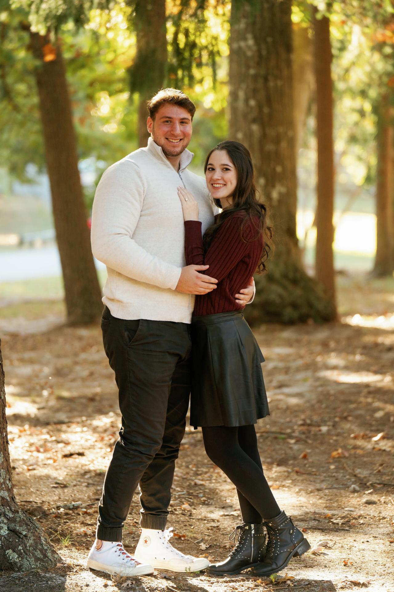 Full-length engagement portrait of a couple among sunlit woodland trees