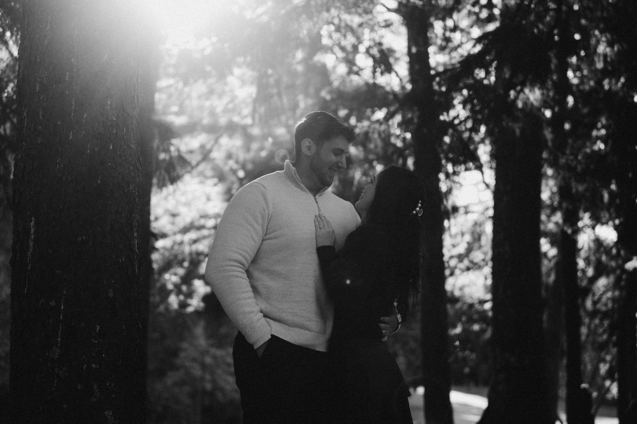 Black-and-white portrait of a couple sharing a kiss beneath the trees