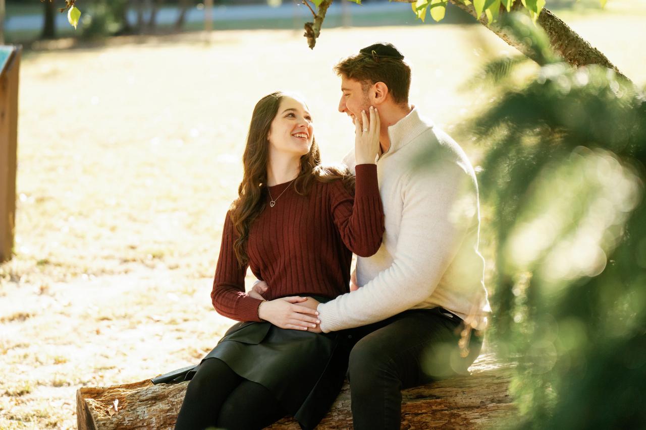 Couple seated together and sharing a smile beneath autumn branches