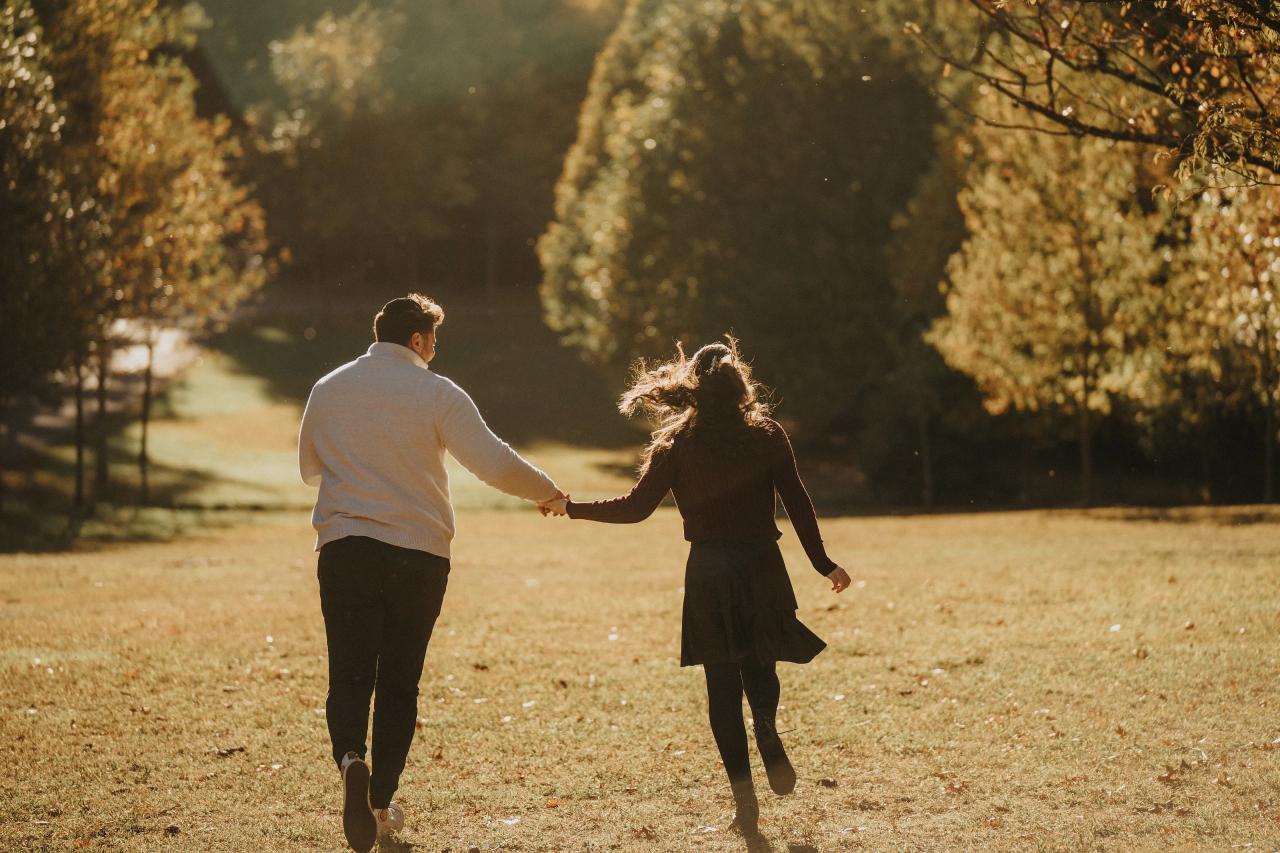 Couple walking hand in hand across a sunlit autumn lawn