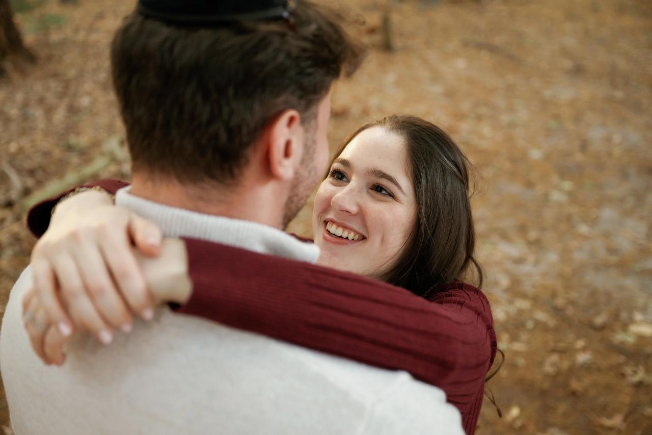 Woman smiling as she embraces her partner beneath autumn trees