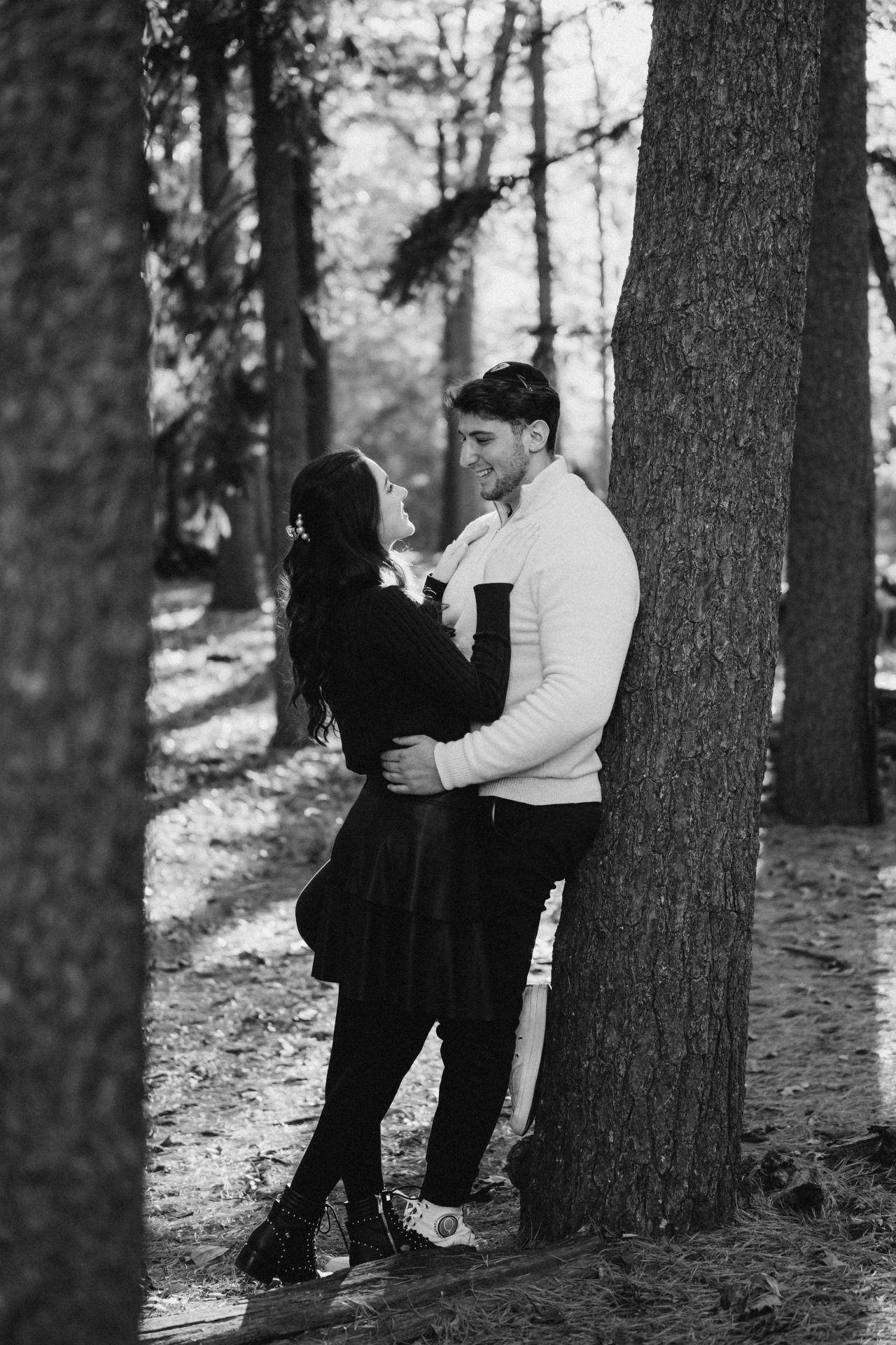 Black-and-white portrait of a couple standing beside a woodland tree