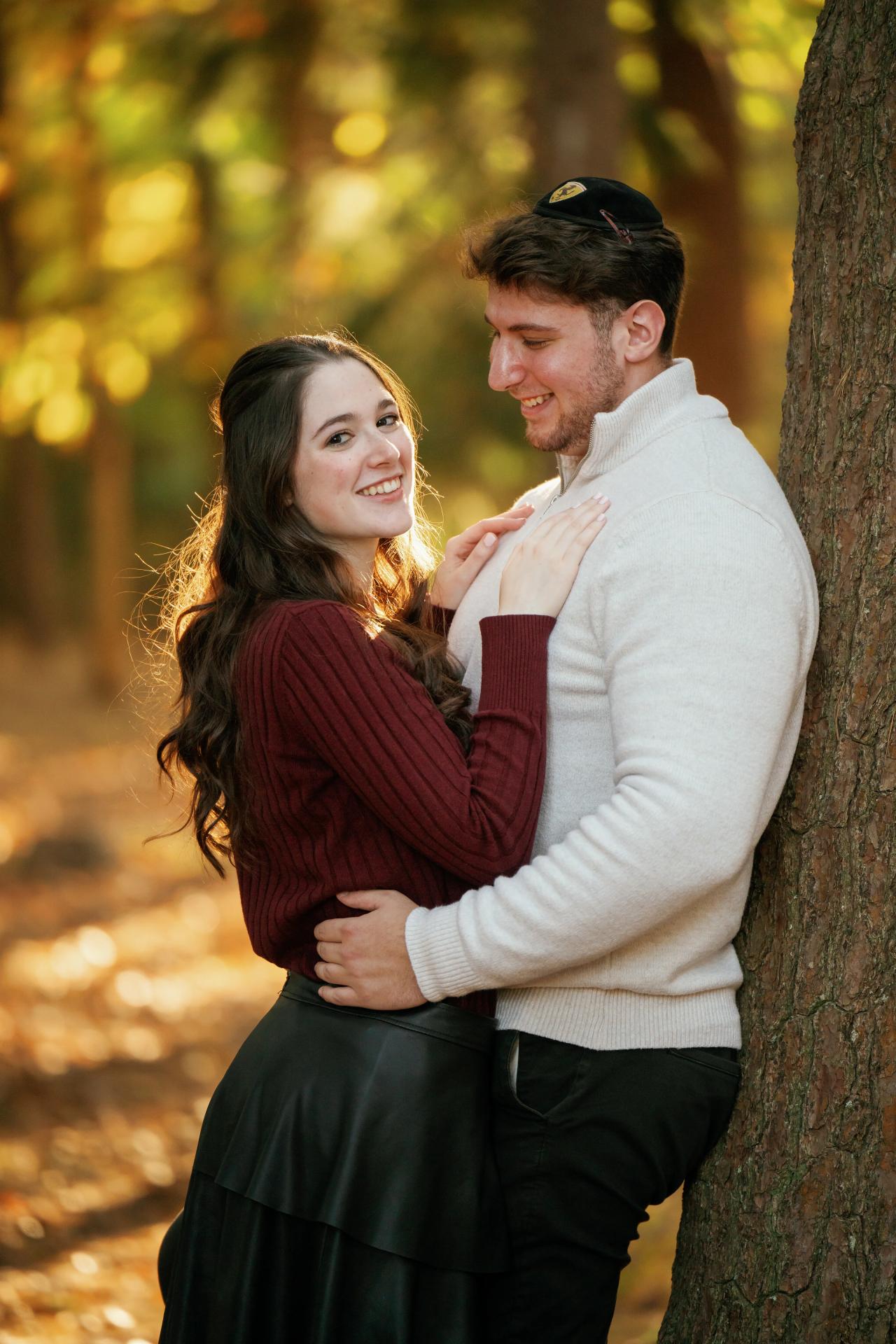Couple leaning together beside a tree during autumn engagement portraits