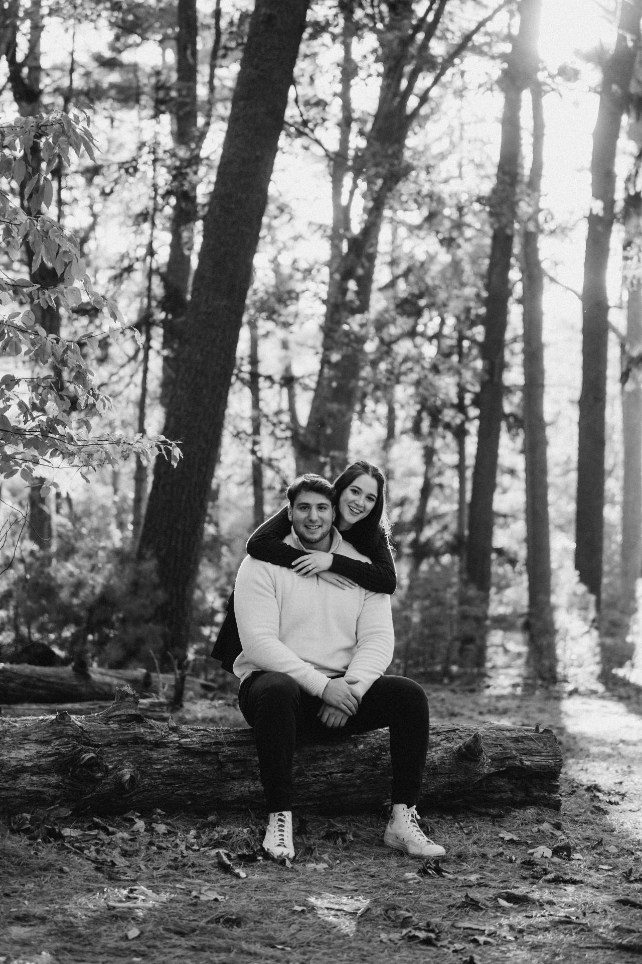 Black-and-white portrait of a couple sharing a piggyback embrace in the woods