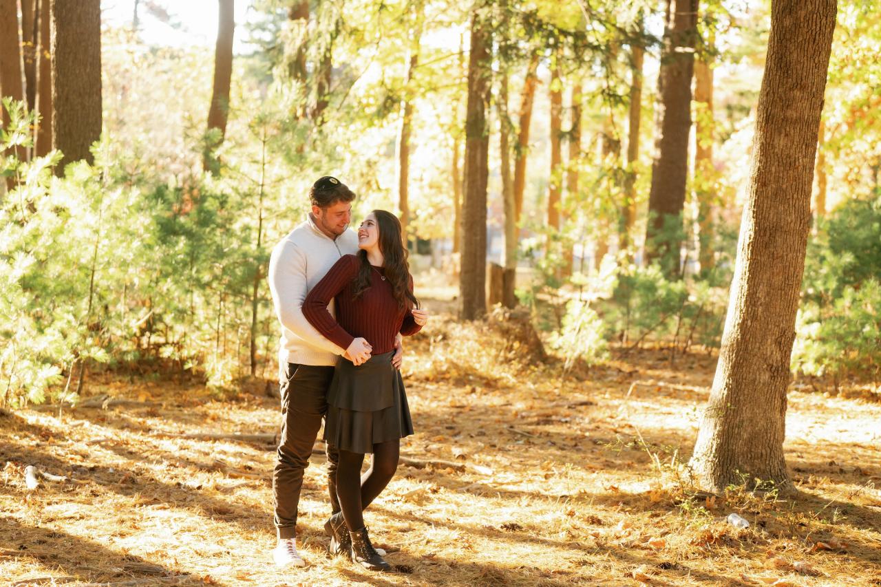 Wide engagement portrait of a couple surrounded by sunlit woodland