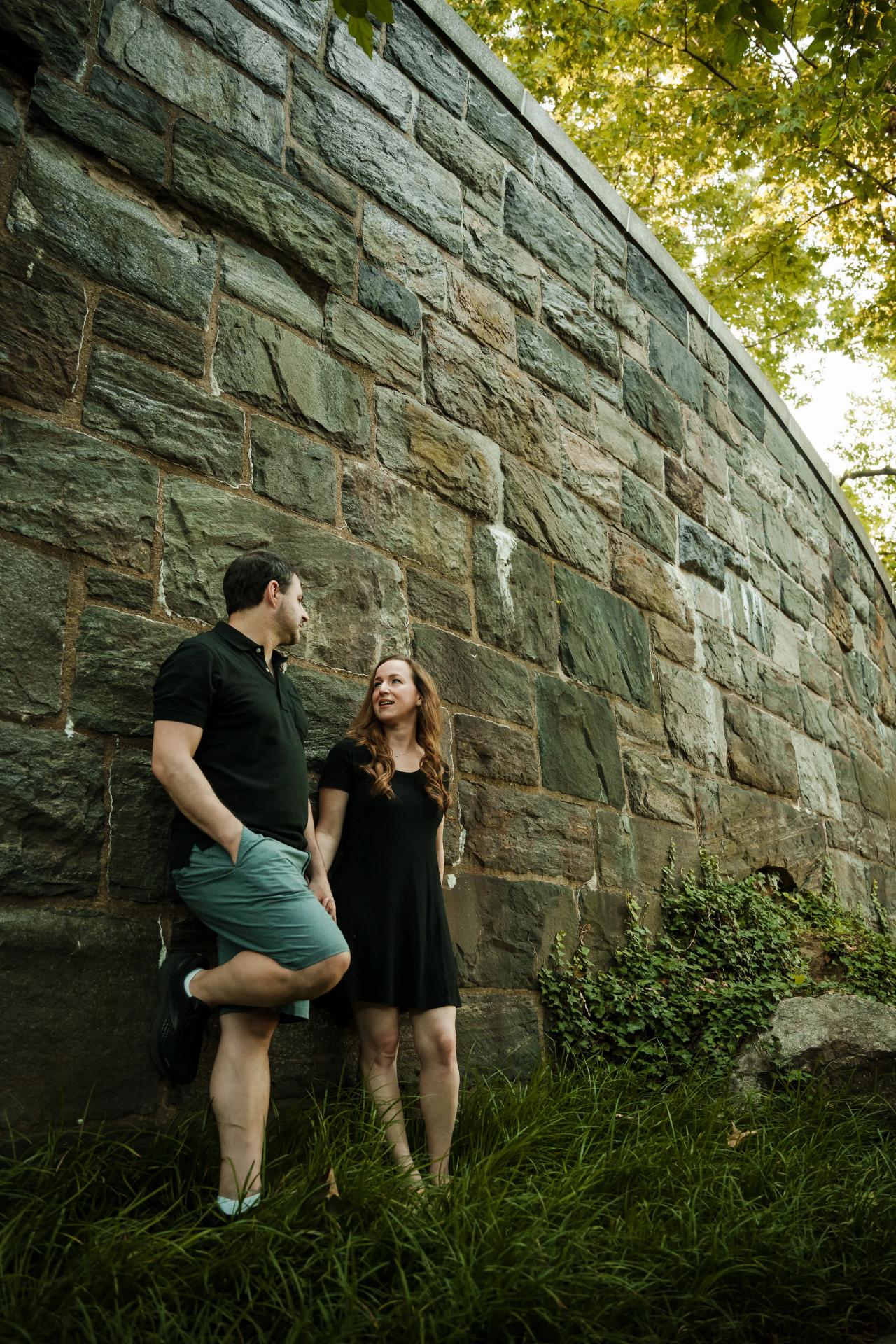 Full-length portrait of a couple beside a stone wall on a leafy path