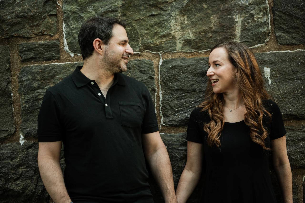 Couple laughing together while holding hands beside a stone wall