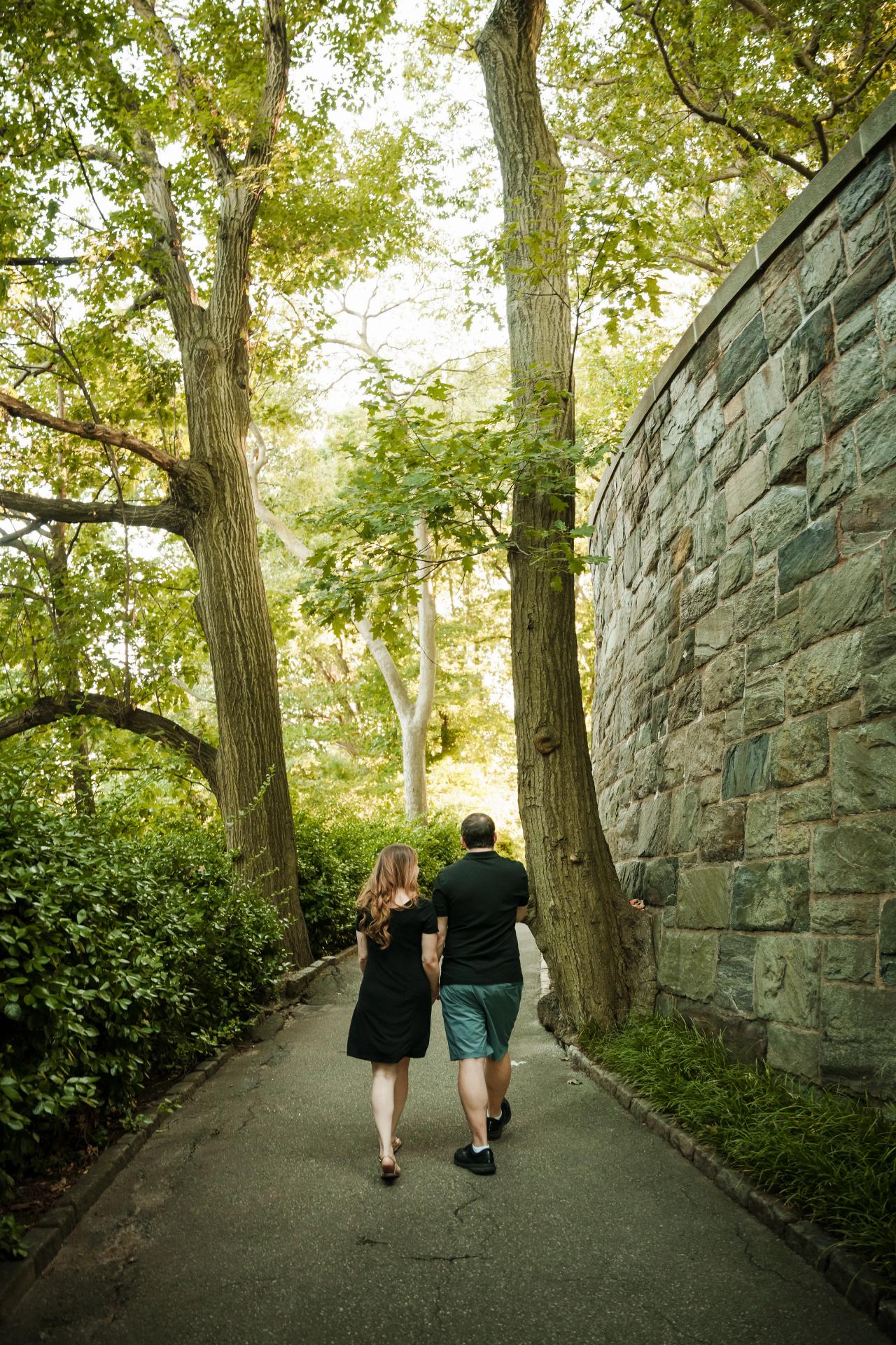 Couple walking hand in hand along a shaded path beside a stone wall