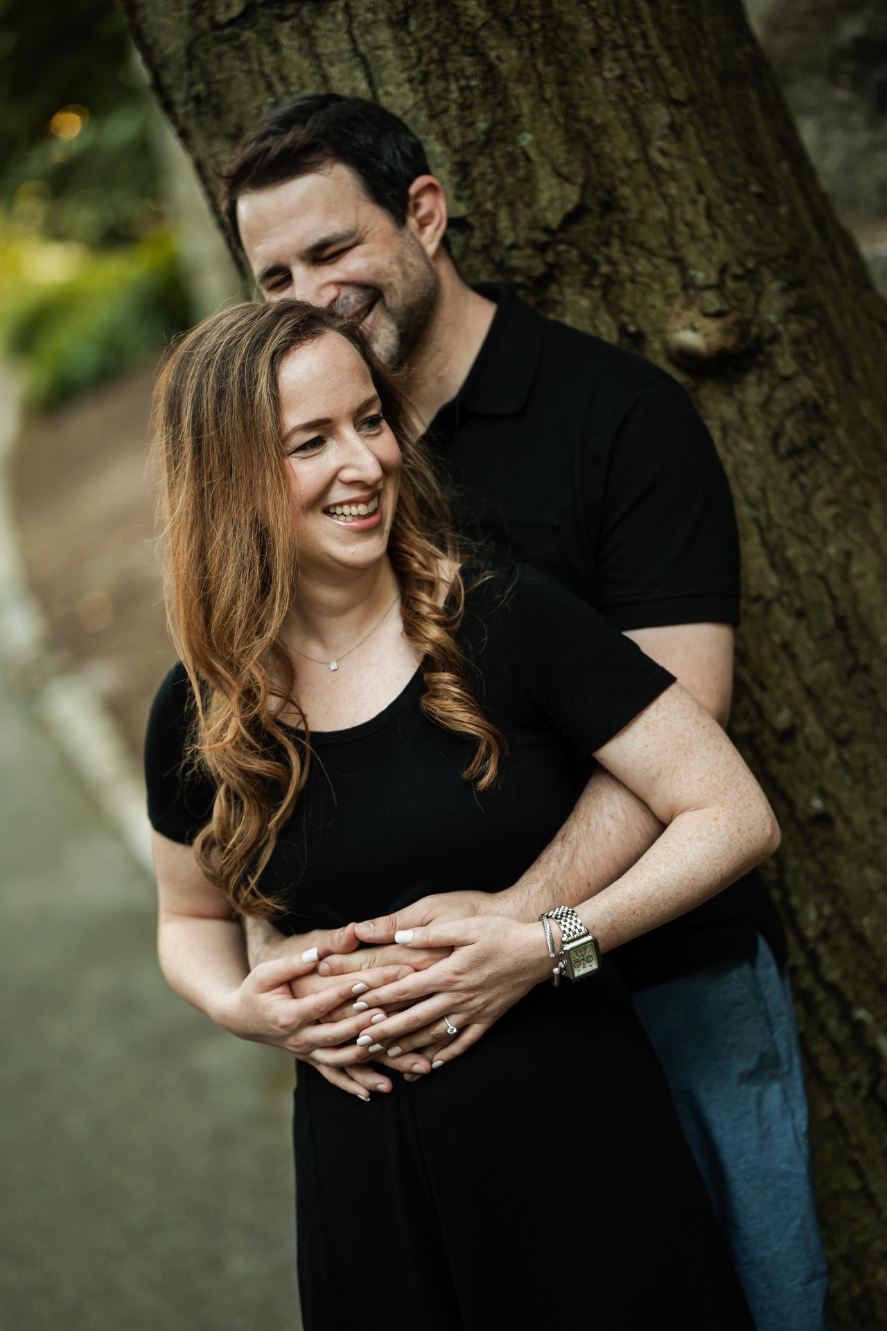 Man embracing his partner beside a tree during an outdoor engagement session