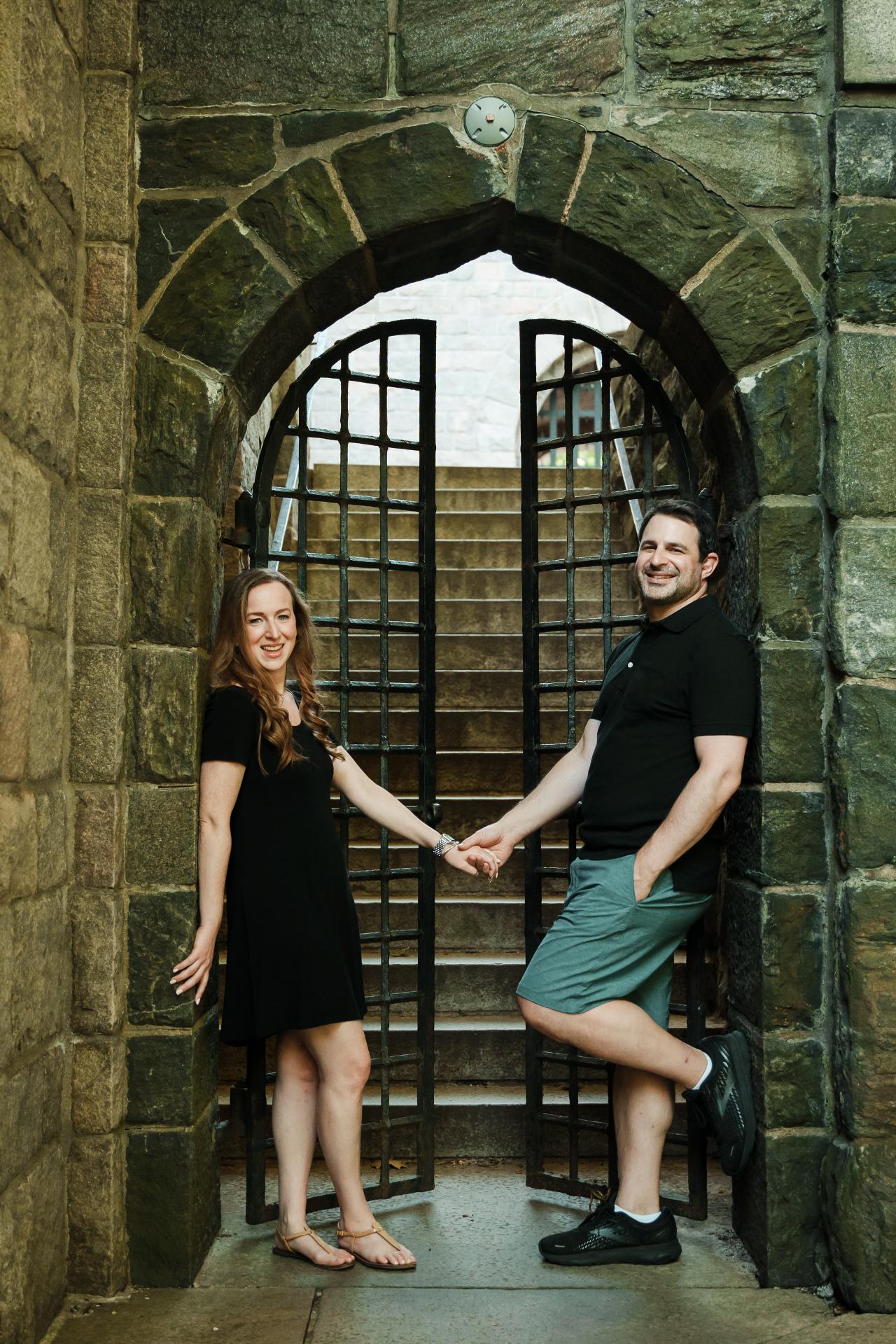 Engaged couple holding hands beneath a stone archway