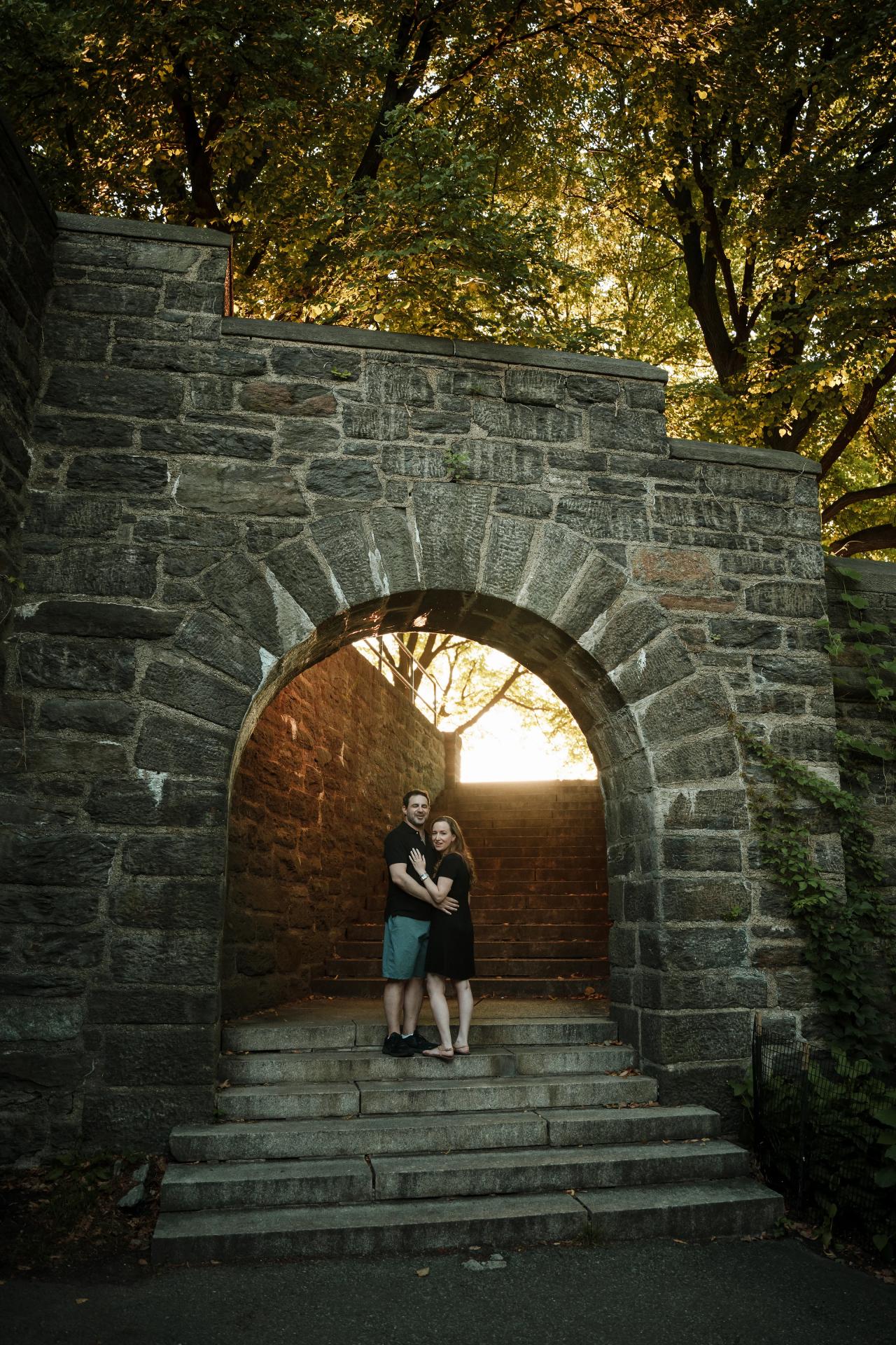 Wide engagement portrait of a couple framed by a stone arch