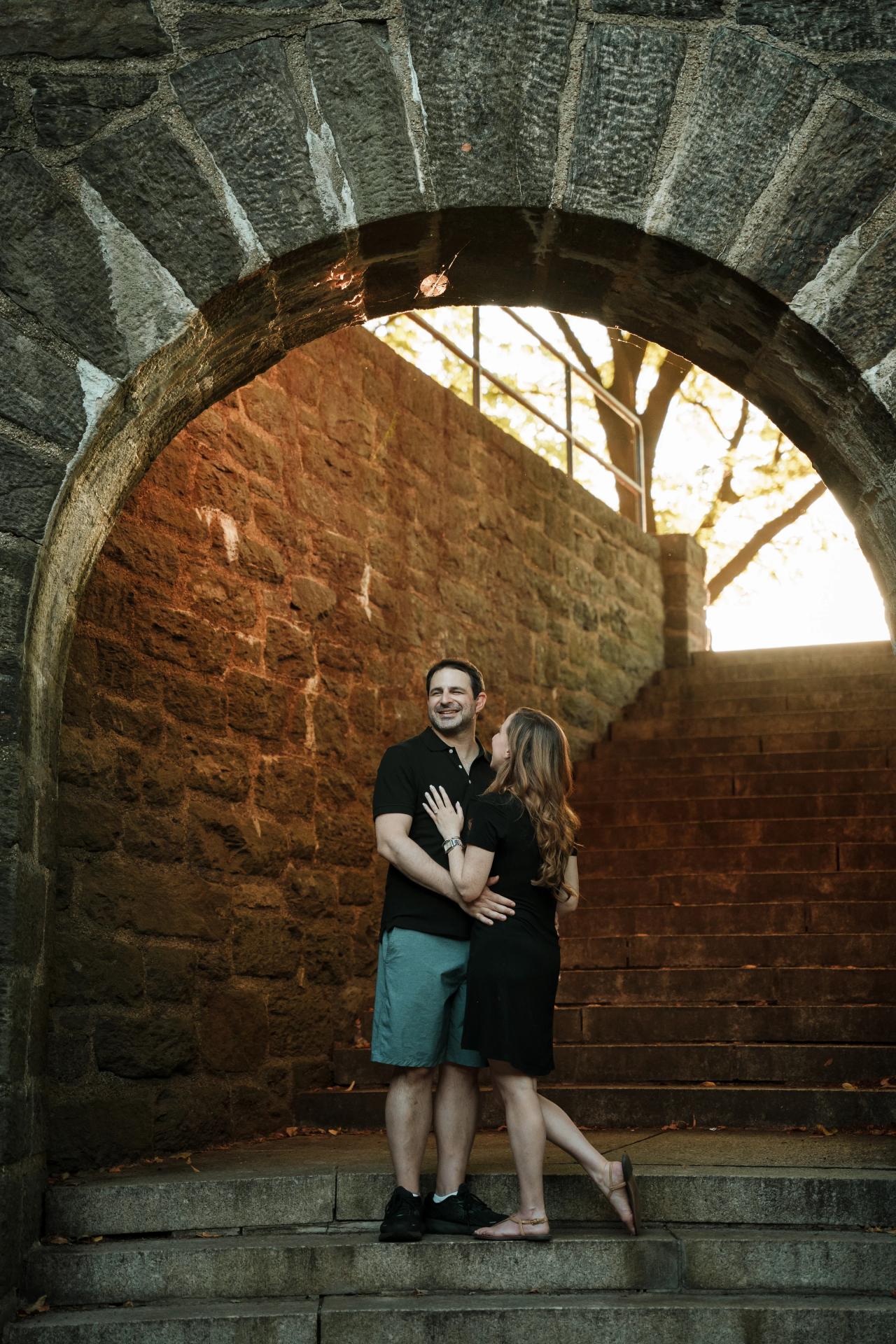 Couple embracing beneath a stone archway in golden evening light